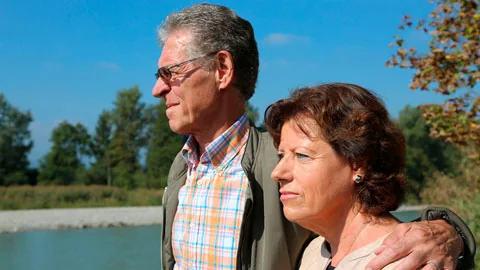 Un homme pose son bras sur l’épaule d’une femme, devant un paysage de campagne.